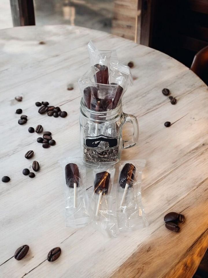 Jar of handmade coffee candy lollipops displayed with coffee beans on a wooden table