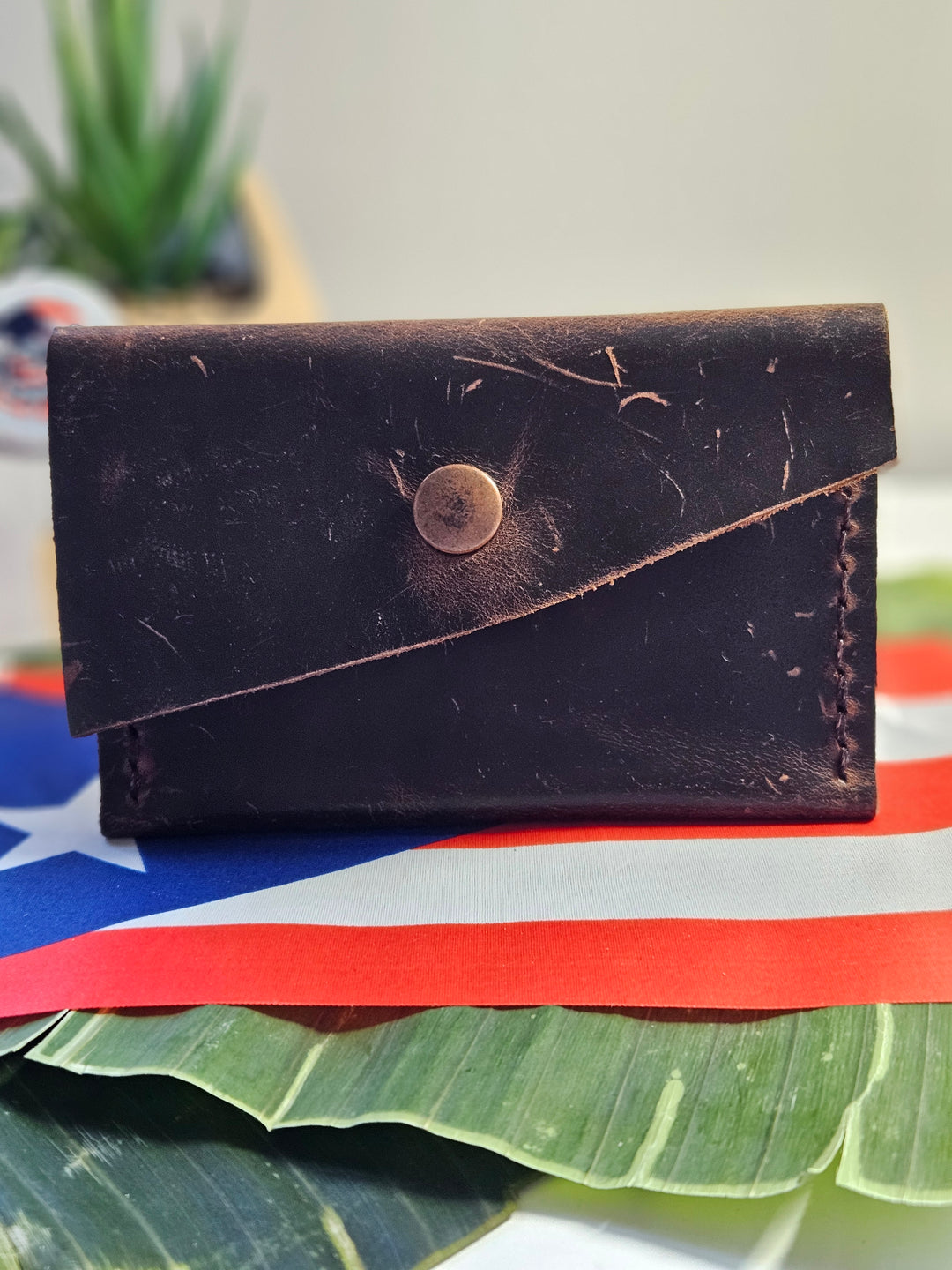 Rustic leather mini wallet by Atelierry, featuring a stylish design and snap closure on a tropical background.