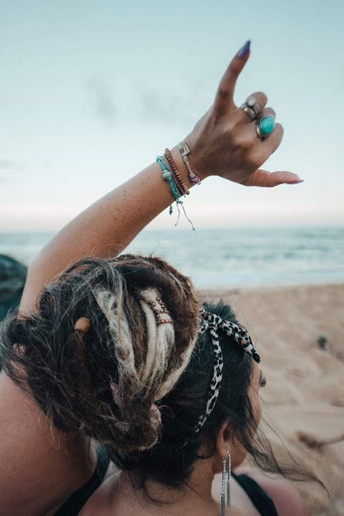 Stylish woman showcasing an alien friendship bracelet handmade along with layered jewelry on a beach