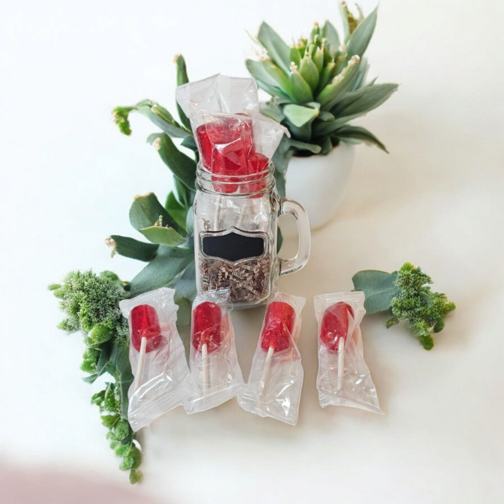 Artisan strawberry lollipops in a jar surrounded by decorative greenery for a delightful gift option