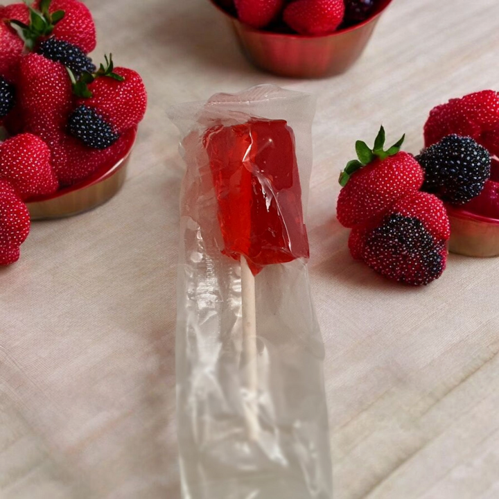 Artisan strawberry lollipops wrapped in clear packaging with fresh strawberries in the background