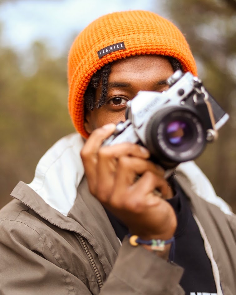Person wearing an orange beanie holding a camera and showcasing an autism puzzle piece bracelet