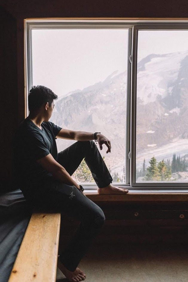 A person gazing out of a large window wearing an autism puzzle piece bracelet, with a scenic mountain view