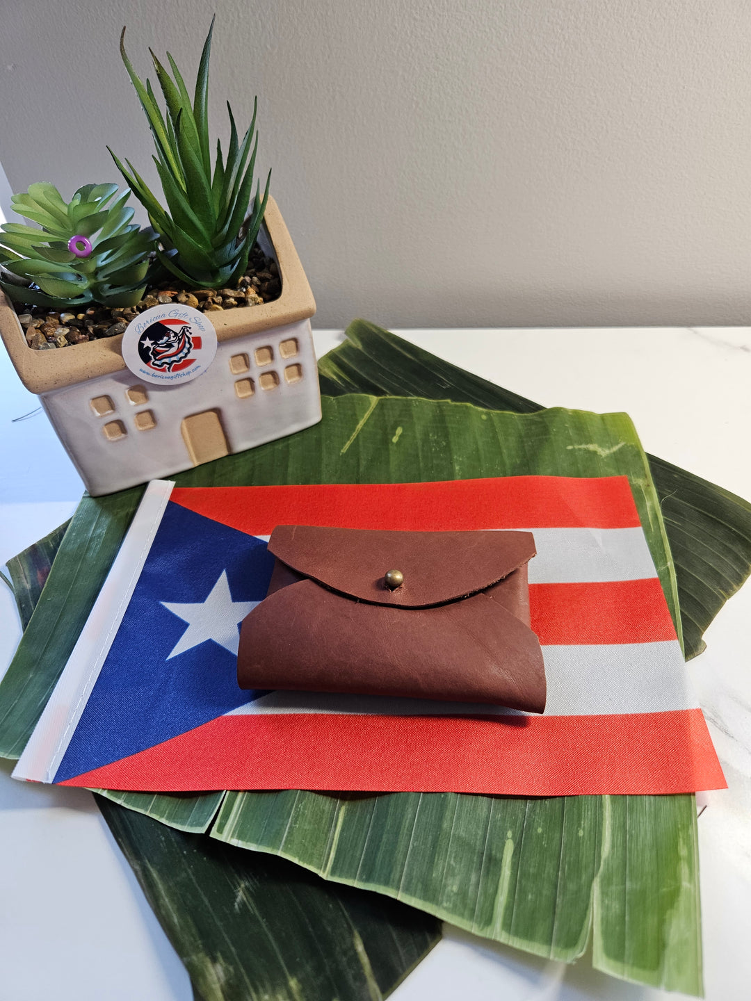 Brown leather pouch gift displayed on a Puerto Rican flag and tropical leaves backdrop
