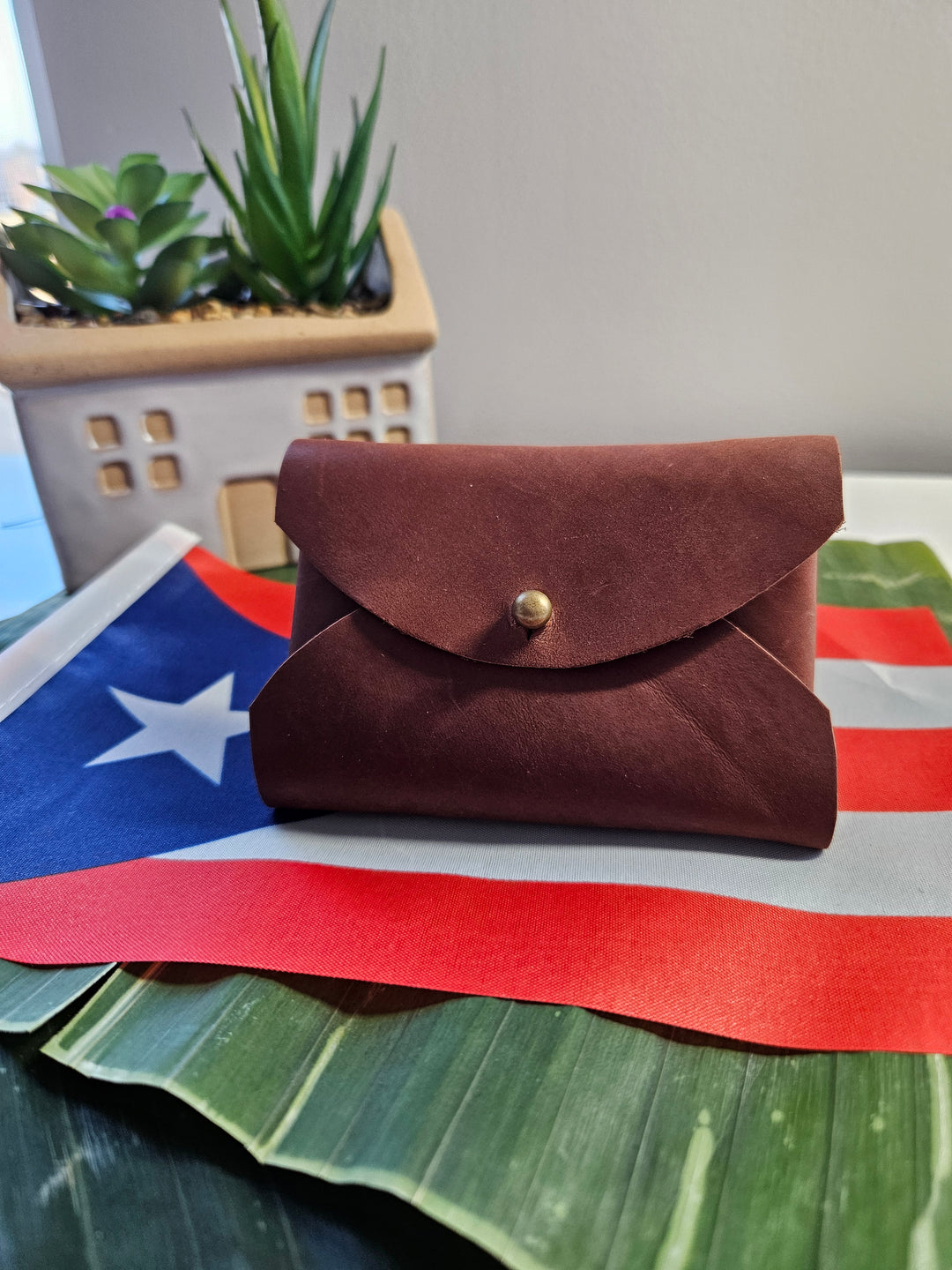 Brown leather pouch gift with brass snap closure displayed on a vibrant Puerto Rican flag backdrop
