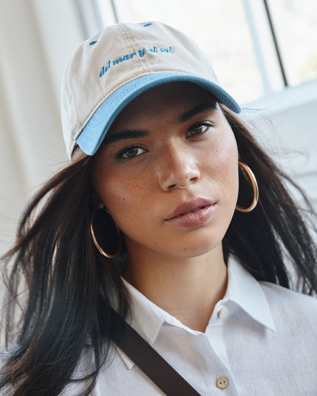 Valija Del Mar Y El Sol souvenir cap in light blue and white worn by a model with hoop earrings