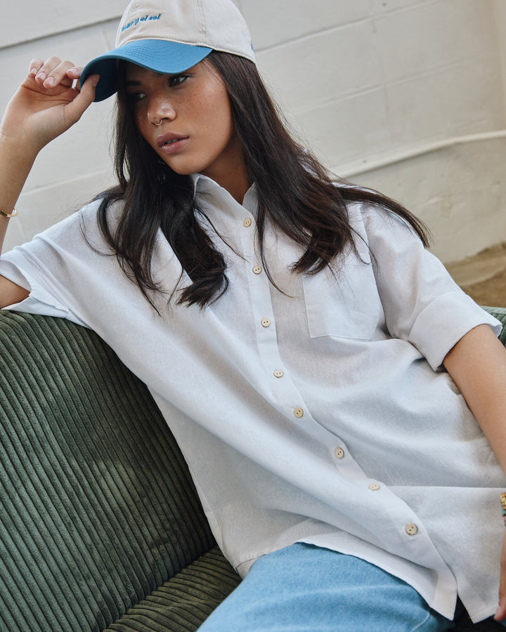 Stylish woman wearing Del Mar Y El Sol souvenir cap with casual outfit, sitting on a green couch