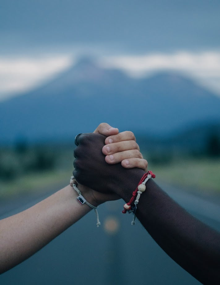 Two hands clasped together wearing a handmade Puerto Rican encouragement bracelet showcasing unity and support