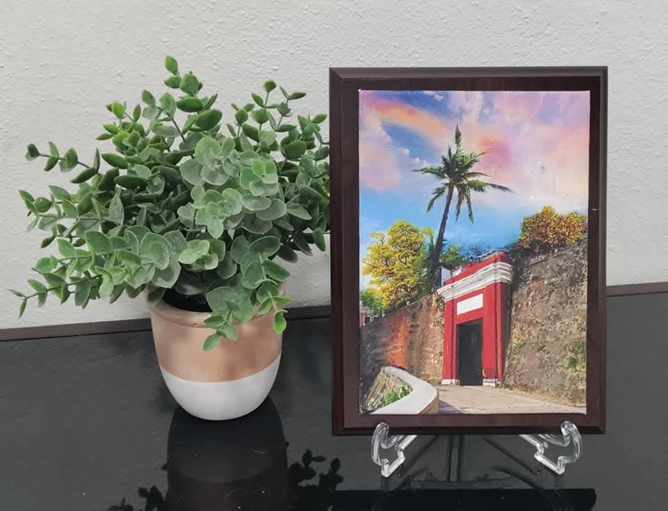 La Puerta del Viejo San Juan painting by Jamie Thomas Art Studio displayed on a stand next to a potted green plant