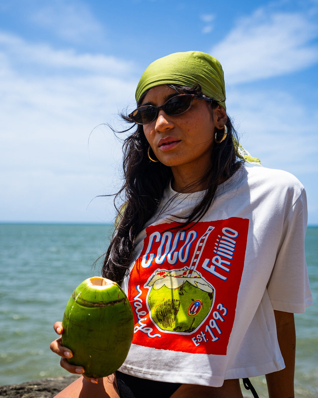 Woman wearing Valija La San Juan Top with coconut drink by the beach under sunny skies