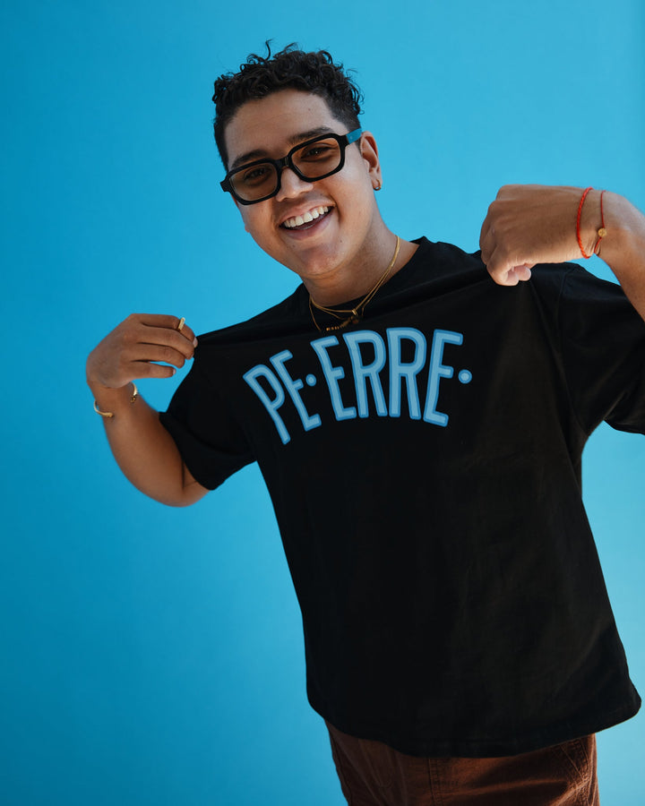Model wearing a black PE ERRE t-shirt with a bold blue graphic design on a bright background