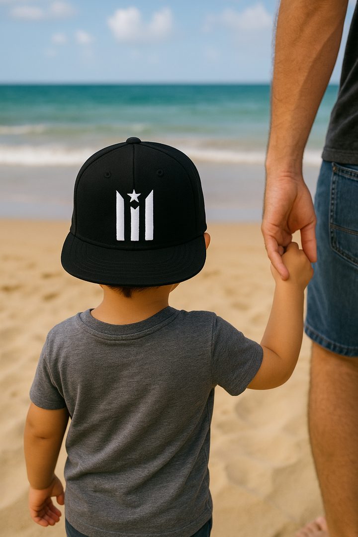 Child wearing a Puerto Rican flag snapback hat while holding an adult's hand at the beach