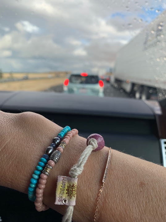 Hand wearing a colorful Puerto Rican happiness bracelet among other beaded bracelets in a car setting