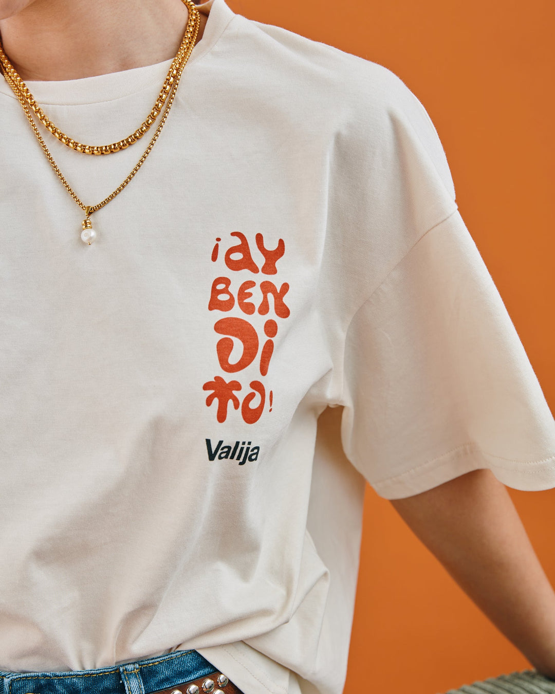 Cream Valija Ay Bendito graphic T-shirt with colorful lettering on a model against an orange background