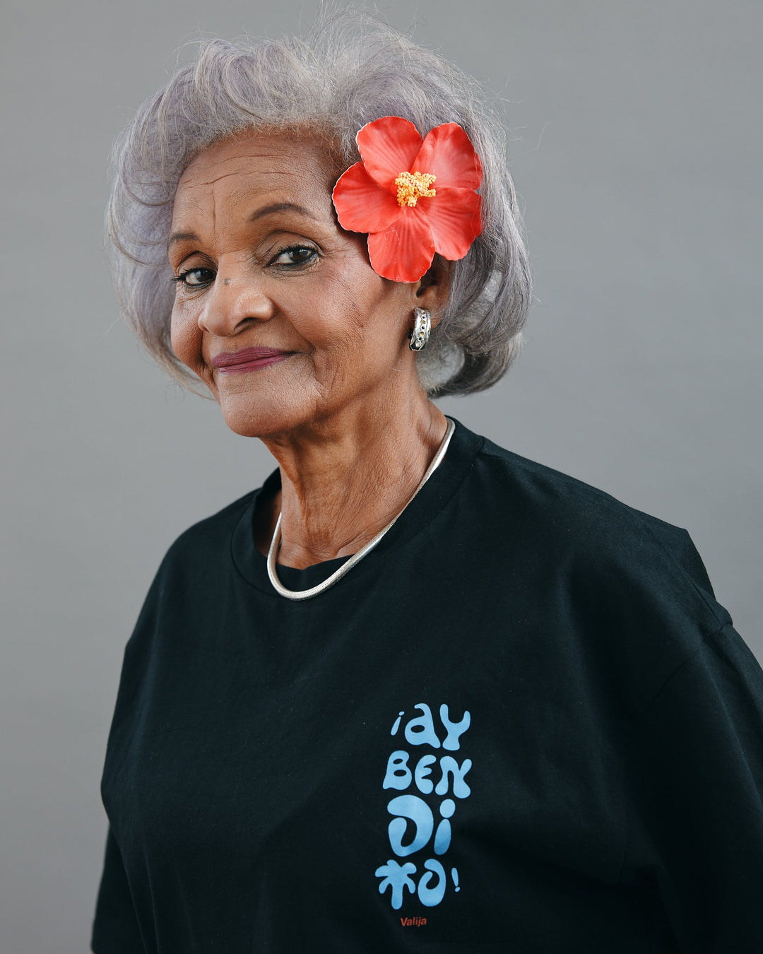 Valija Ay Bendito graphic T-shirt in black displayed on a model with gray hair and floral accessory